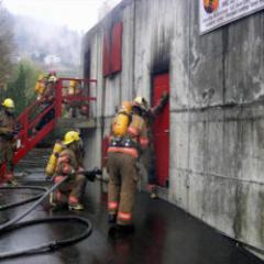 Firefighters with hose in front of smokey concrete building